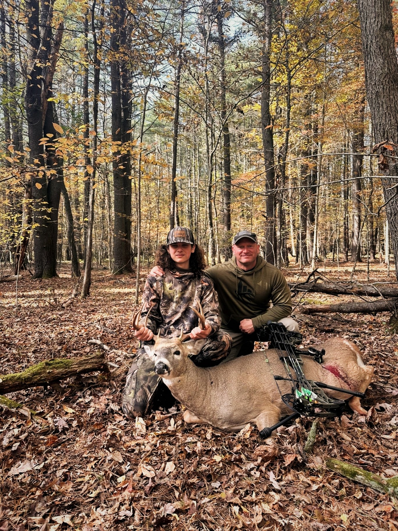 Anthony DelVecchio and a young hunter with a bow-harvested whitetail buck in fall timber