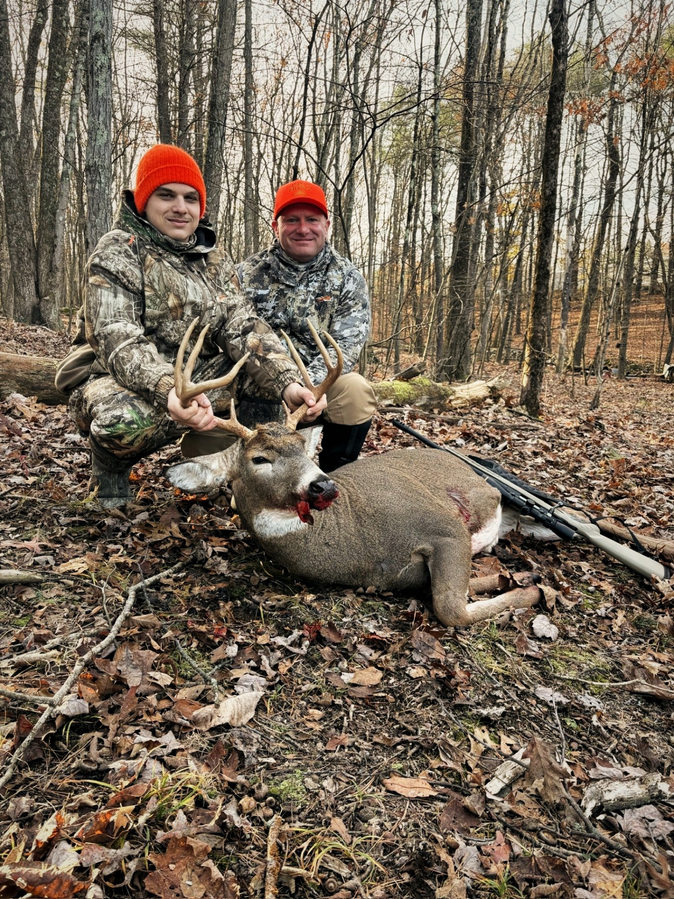 Two hunters kneeling behind a harvested whitetail buck during rifle season
