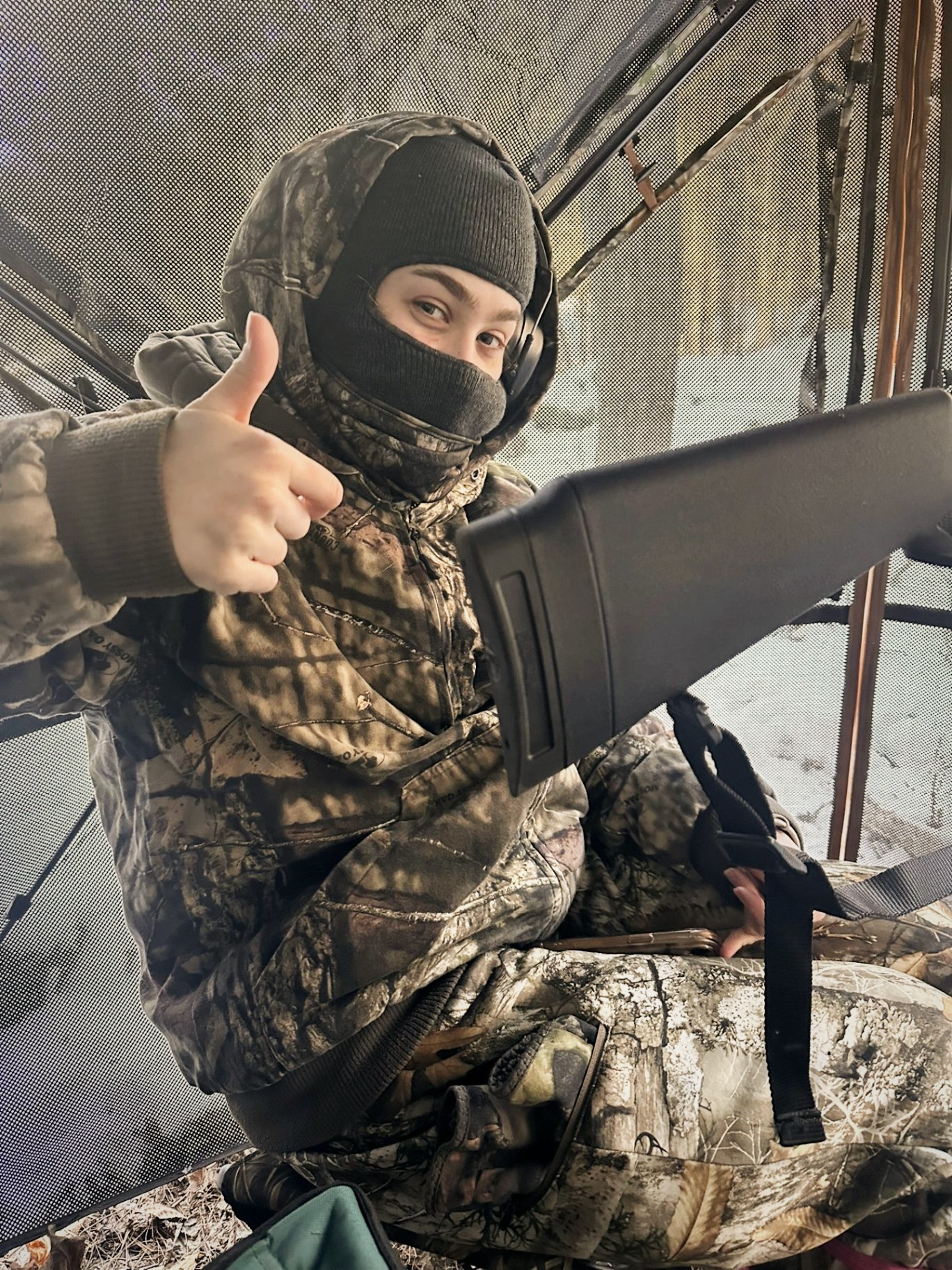 Young hunter in camo giving a thumbs up from inside a ground blind