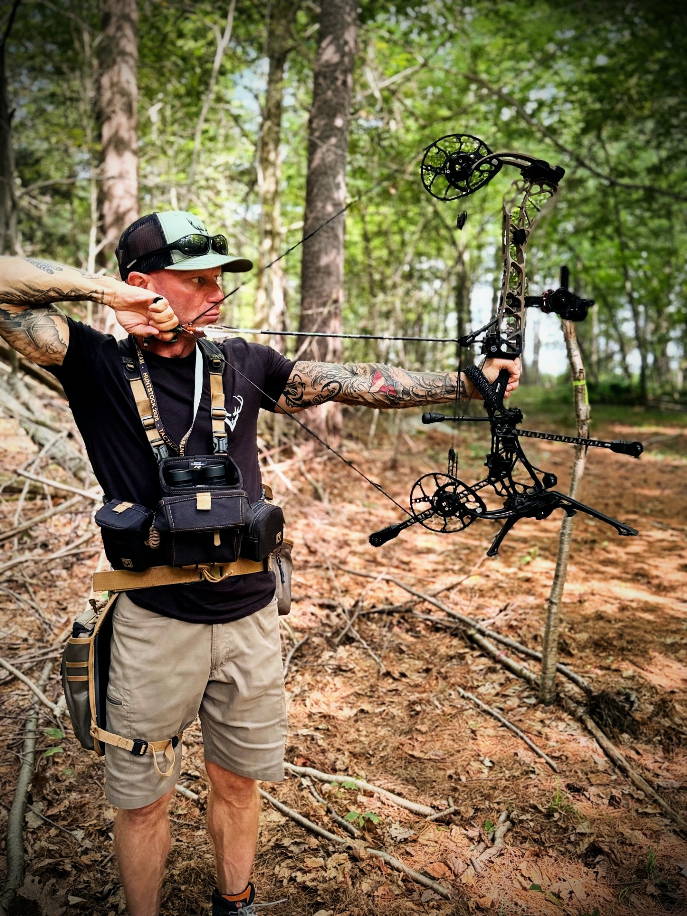 Anthony DelVecchio at full draw with his compound bow in green summer timber