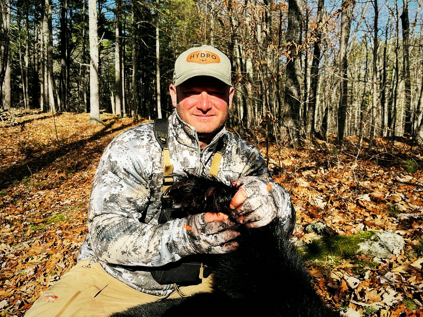 Hunter holding the paw of a harvested black bear in the timber