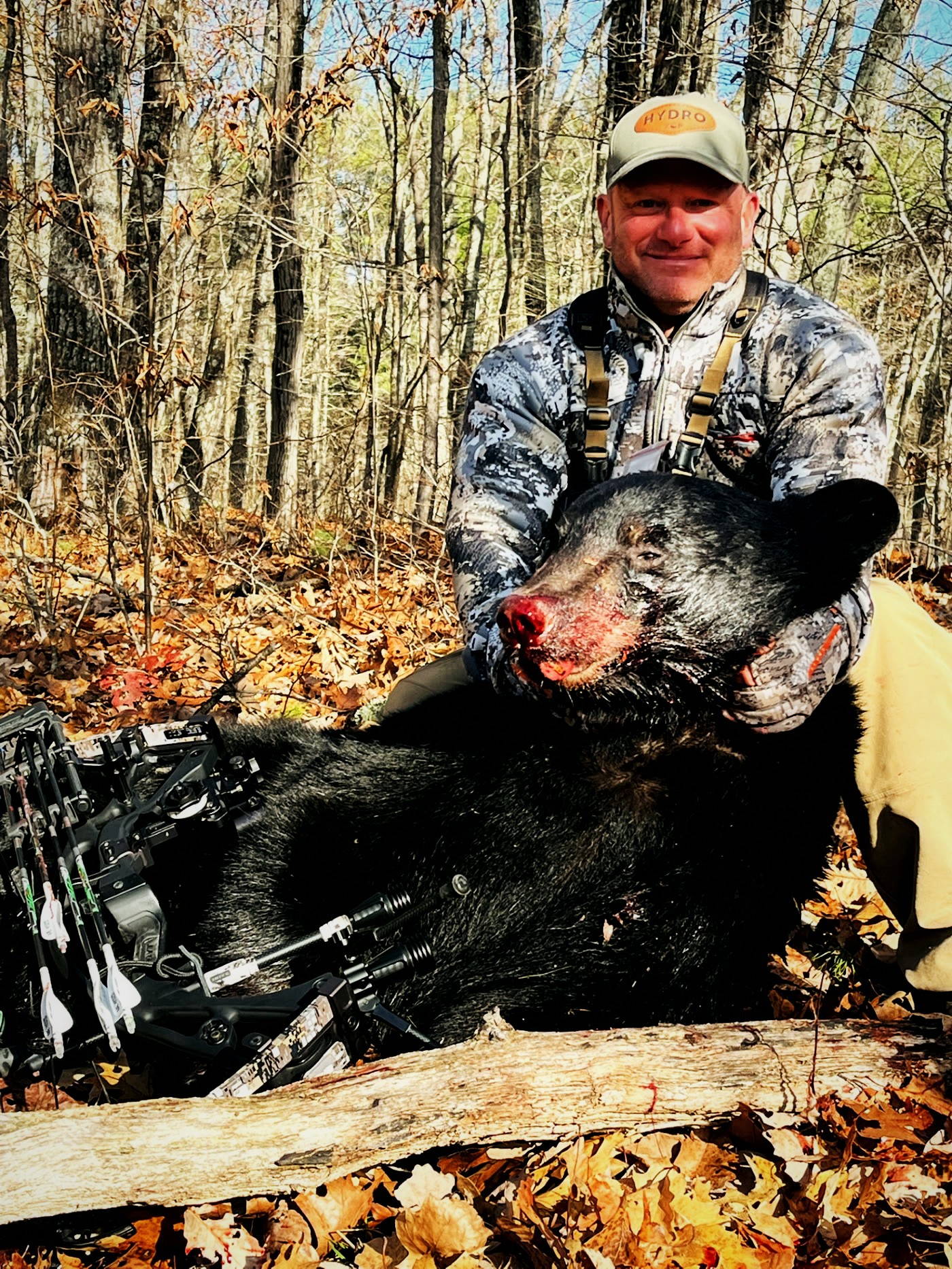 Hunter kneeling behind a harvested black bear in autumn hardwoods
