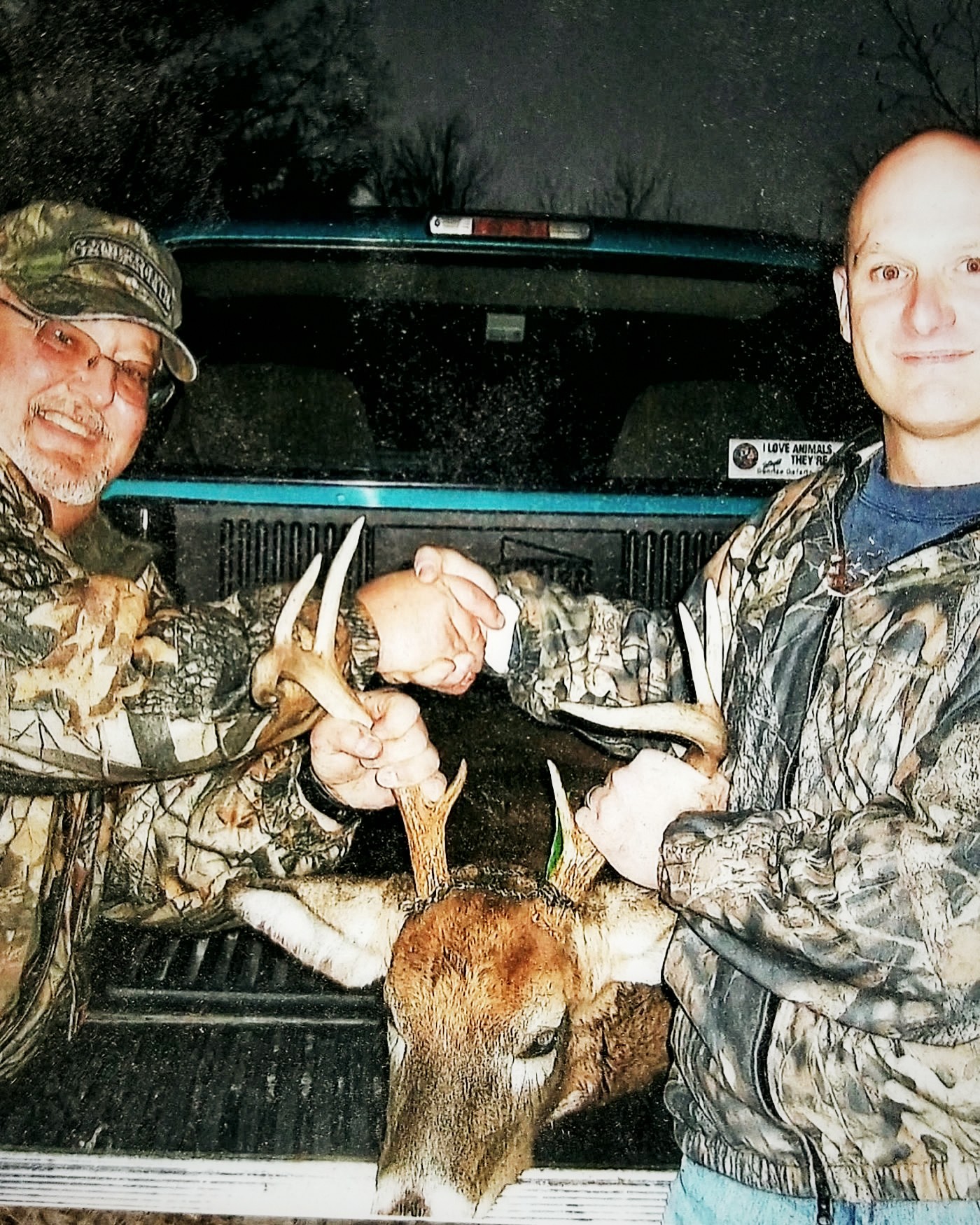 Two hunters shaking hands over a whitetail buck on a truck tailgate