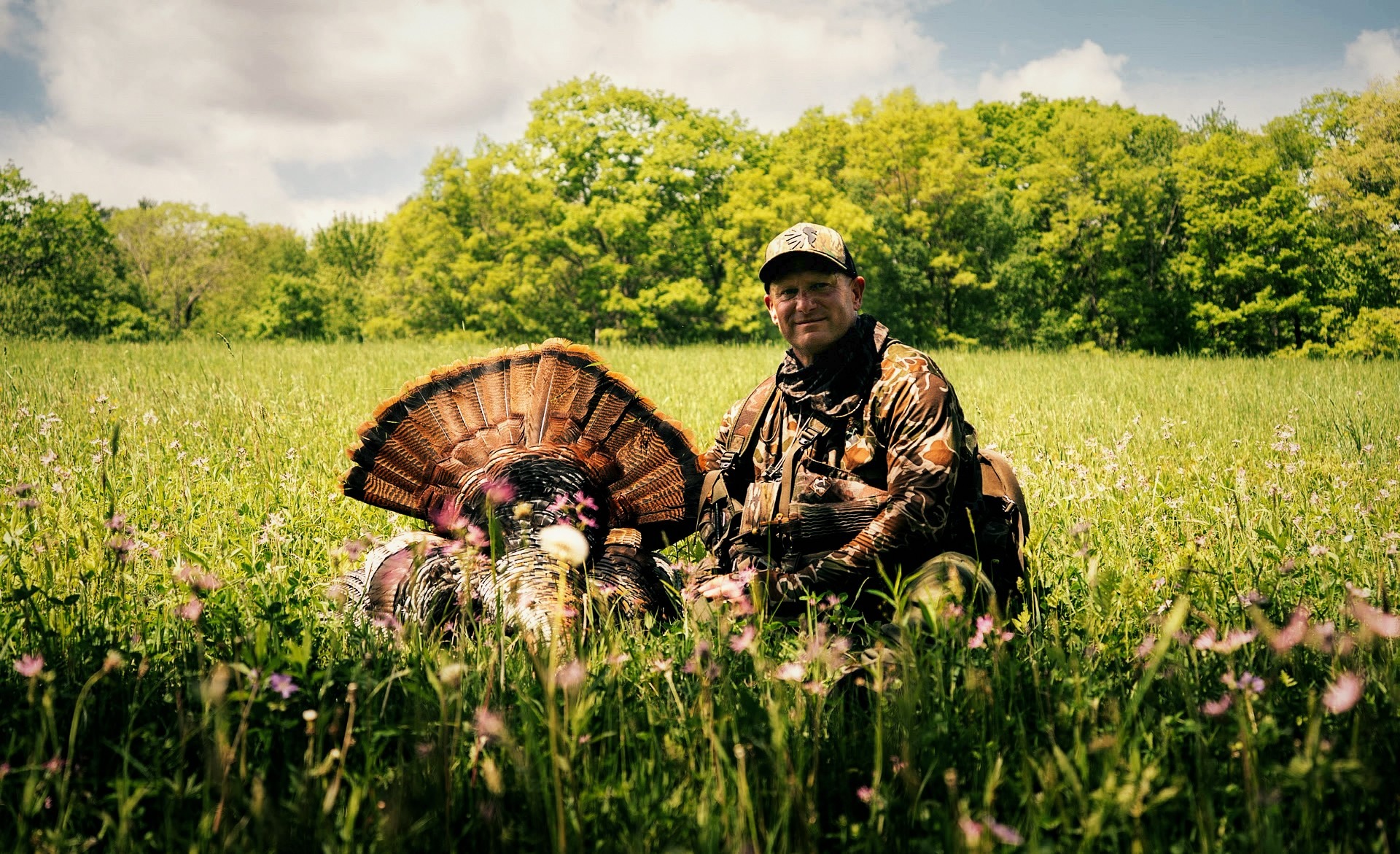 Hunter kneeling in a spring meadow with a harvested wild turkey fanned out
