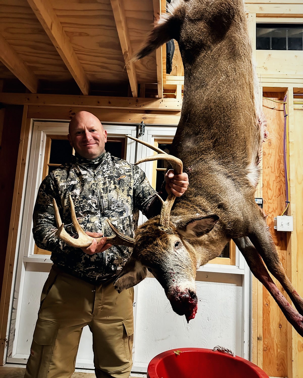 Hunter holding the rack of a heavy hanging whitetail buck